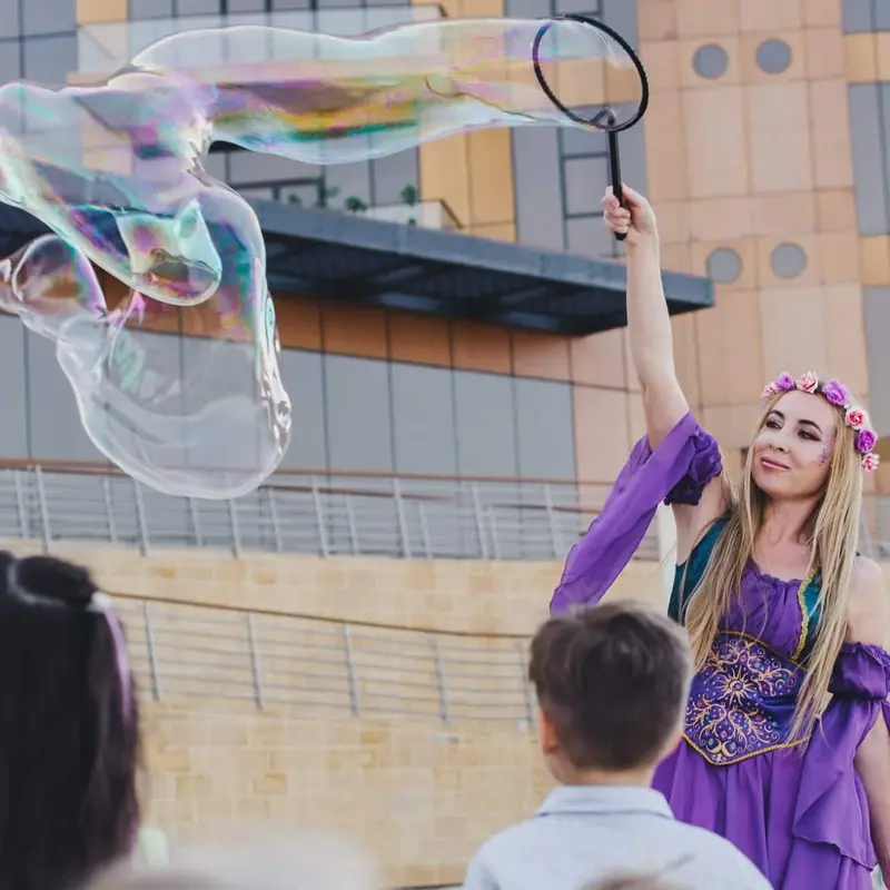 Bubble performer in a purple costume lifting a giant soap bubble over children at an outdoor kids event in Dubai