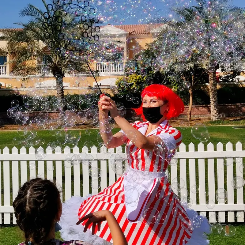 Bubble performer in a red and white striped dress filling a garden with bubbles at a kids party in Dubai
