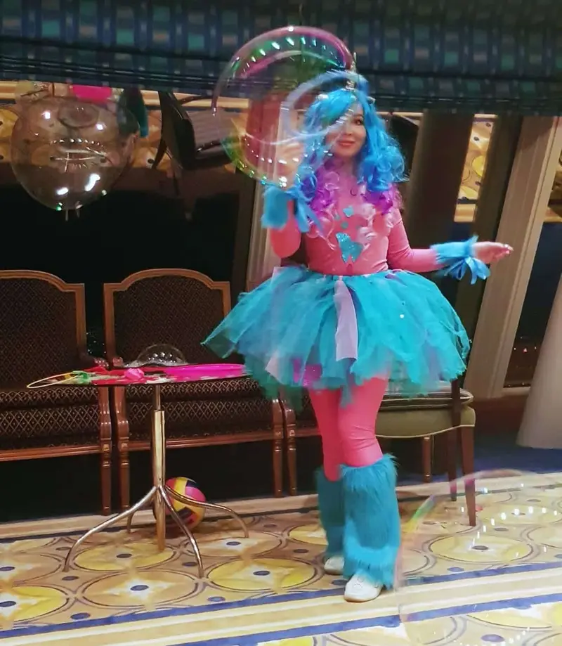 Kids entertainer in a unicorn costume with a turquoise tutu making bubbles at an indoor party in Dubai